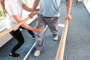 Physiotherapist,Helping,Senior,Man,In,Rehabilitation,Walking,On,The,Bars